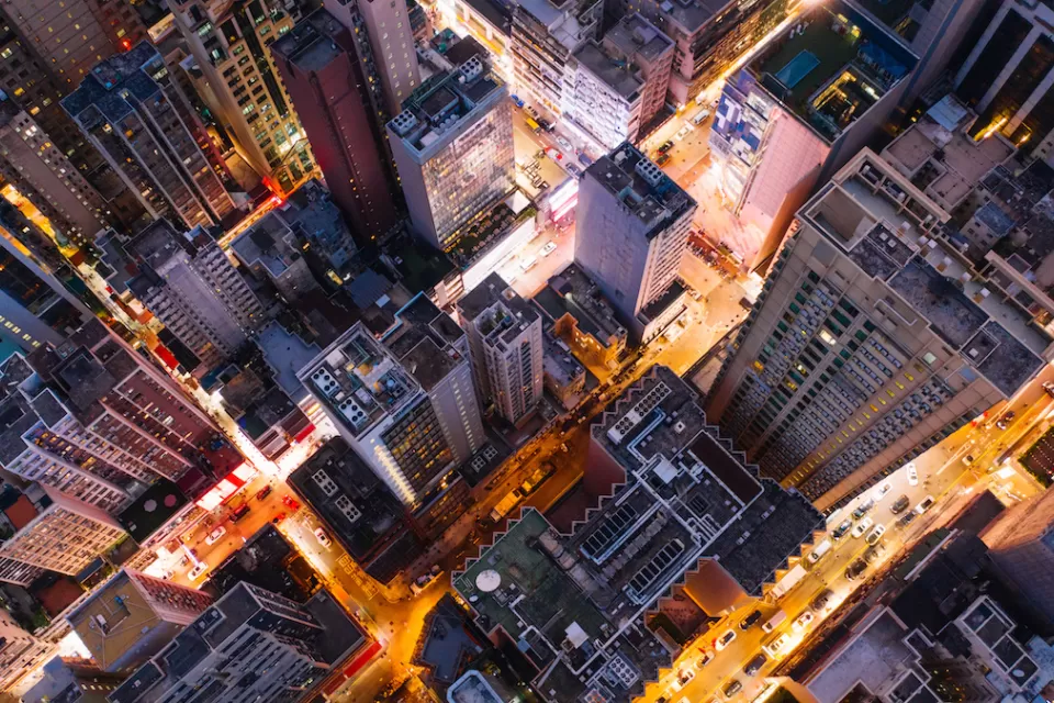 Bird's eye view of city skyscrapers at twilight with blurred lights on streets.